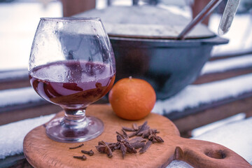 Hot mulled wine in a glass on a wooden board with anise, cinnamon and tangerine. A warming Christmas or winter drink prepared on a frosty street.