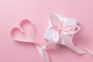 Gift box and ribbon in the shape of a heart on a pink background. Valentine's day concept.