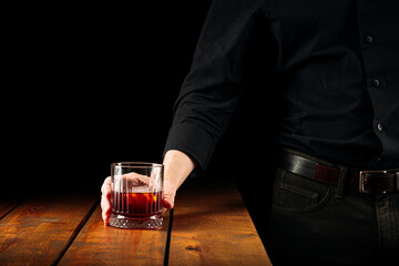 Man holding a glass of negroni cocktail above the wooden table