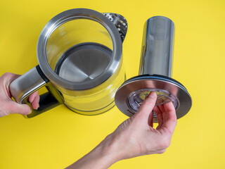 electric metal kettle in silver color with different modes of water heating on a bright yellow background. A woman's hand holds a piece for brewing tea. Side view
