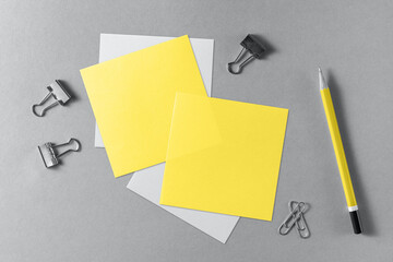 Yellow blank sheets of note paper and a wooden pencil on a grey background.