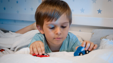 Smiling little boy playing with two toy cars while lying in bed at night. CHild playing before going to sleep. © Kyrylo Ryzhov