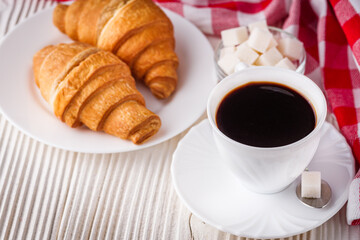 delicious fresh croissant and cup of coffee on a white wooden rustic background