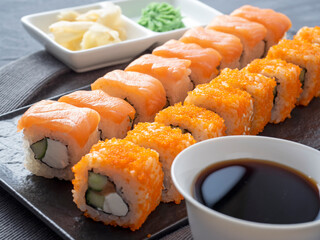 Philadelphia and California rolls on a textured dark plate. Next to soy sauce, wasabi and ginger. Side view, close up. Japanese cuisine