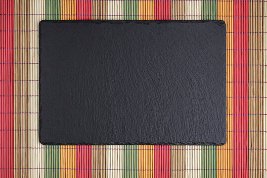 Top view of black stone platter on multicolored bomboo mat background with copyspace