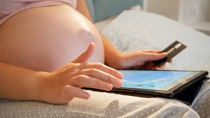 Closeup of pregnant woman with big belly holding credit card and browsing online store. Pregnant doing online shopping