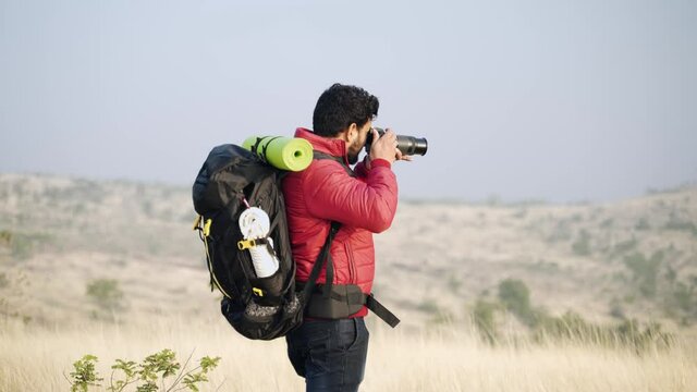 young hiker or traveller with backpack entering the scene taking picture of landscape using camera - concept of travel and aventure photography while trekking.
