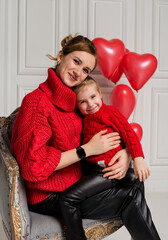 Beautiful mother and daughter sitting and hugging in a chair on a white background with red balloons