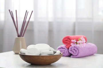 Fototapeta na wymiar Spa stones, towels and reed freshener on white table indoors