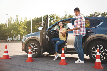 Instructor with clipboard and his student near car outdoors. Driving school exam