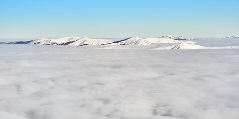 Fototapeta na wymiar Sea of clouds in Winter, above Sinaia ski resort in Romania, with snow covered Carpathian mountain peaks in the distance. Temperature inversion, cloud inversion. 