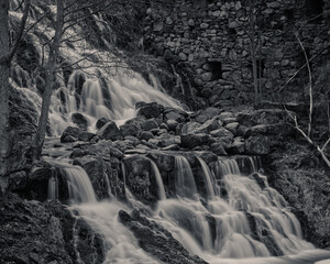 Black and white image of a waterfall with a stone building in the background