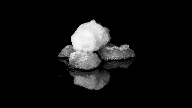 Three snowballs melting on black reflective surface, time-lapse studio shot