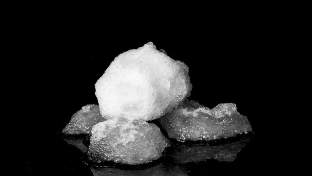 Three snowballs melting on black reflective surface, medium shot