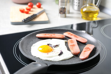 Egg and sausages in frying pan on stove indoors