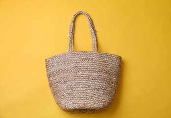 Stylish straw bag on yellow background, top view. Summer accessory