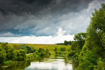 Forest, river and large black clouds before the rain. summer day