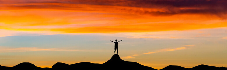 Silhouette tourists standing on top of a mountain peak, panoramic sunset views.The symbol...