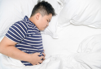 Top view of asian child suffering from stomachache and lying on bed.