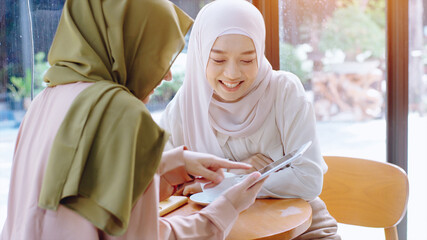 Young beautiful Asian Muslim women enjoying a relaxing moment working and playing with mobile phone in the coffee shop on a bright sunny day