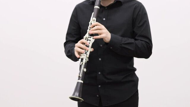 Male hands playing clarinet on white background. Man dressed in black clothes, no face, holding black clarinet on white blank wall background