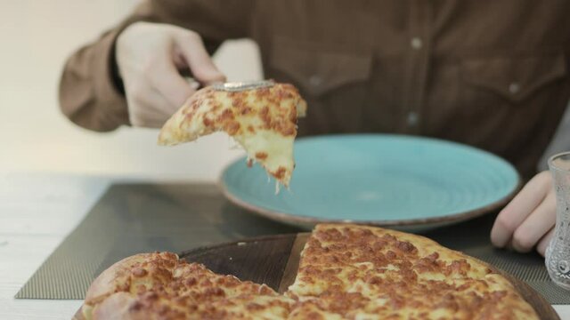Female hand is taking a slice of georgian khachapuri megruli with cheese. Woman with tongs takes a piece of khachapuri from a tray to a plate