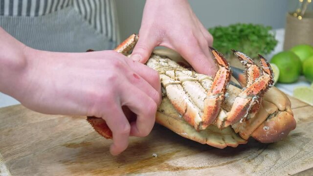 Close-up of eating a crab by pulling off the legs, a twisting motion in 4K. A woman chef is preparing a whole big boiled crab to be eaten on a chopping board on the table.