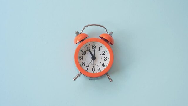 Timelapse video with zoom effect of orange alarm clock on blue background at 11:00 am. 