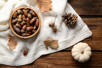 Flat lay composition with acorns, pumpkin and white knitted fabric on wooden table