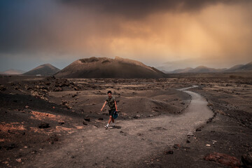 Young man walks along the path of El Cuervo volcano in Timanfaya National Park at sunset. Lanzarote. canary islands