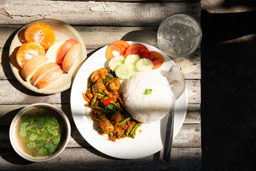 Stir fried chicken and sting bean red curry paste serve with seasonal fruit soup and drinking water on wooden table in high contrast lighting stock photo