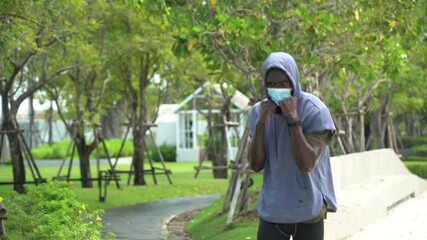 african american young runner man wearing surgical face mask running and practicing punches in park in morning. black male training boxing protective by mask during Coronavirus or Covid-19 pandemic - Powered by Adobe