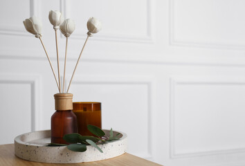 Reed air freshener with candle and eucalyptus branch on tray indoors. Space for text