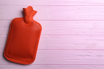 Hot water bottle on pink wooden background, top view. Space for text