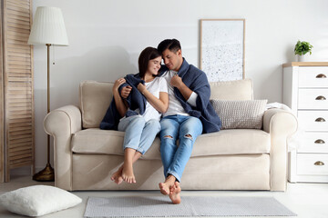 Obraz premium Happy couple in love covered with warm dark blue plaid sitting on sofa at home