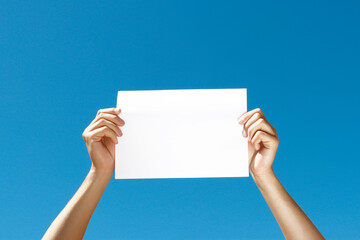 blank sheet of paper in hands on blue background