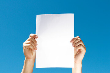 blank sheet of paper in hands on blue background