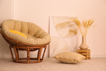 Fototapeta na wymiar Vase with decorative dried plants and painting near papasan chair in stylish room interior