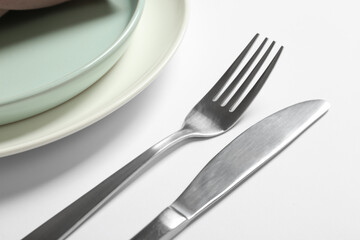 Fork, knife and plates on white table, closeup