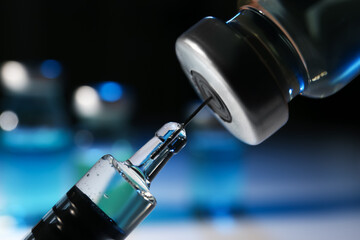 Filling syringe with vaccine from vial on blurred background, closeup