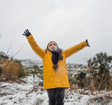 A girl in a yellow jacket playing happily in the snow with her arms raised