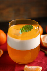 Delicious tangerine jelly in glass and fresh fruits on table, closeup