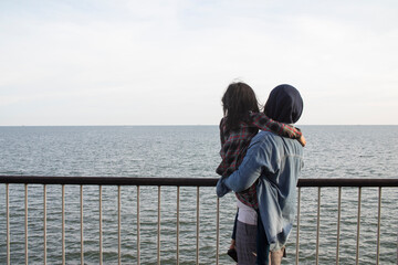 Asian muslim mother and daughter having fun by the sea, family playing outdoor under bright sun