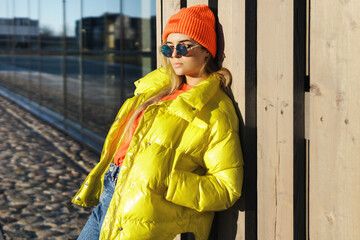 Stylish girl wearing yellow puffer and orange knitted hat