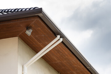 rain gutter and white plastic down pipe with cloudy sky background.