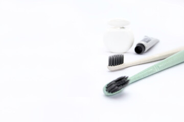 Two pastel color toothbrushes with fine black bristles, white dental floss and a mini tube of...