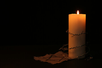 Fabric with star of David, barbed wire and burning candle on black background, space for text. Holocaust memory day - obrazy, fototapety, plakaty