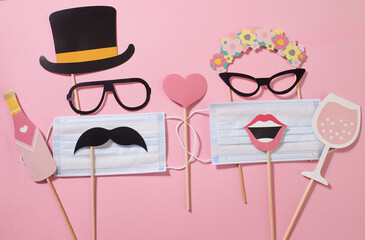 Paper lady and gentleman consisting of sunglasses, hat, mustache, lips with a medical mask, a glass of champagne, bottle on the pink background. Quarantine party. Funny fashion.