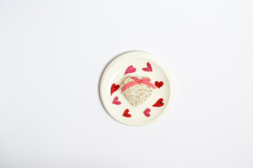 Shiny heart and different decorative hearts on a plate on a white background