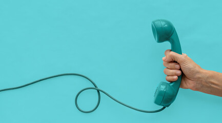 A blue-green vintage dial telephone handset with one hand and blue-green background.  - Powered by Adobe